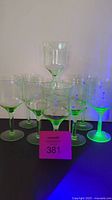 Eight uranium glass wine glasses grouped together with a blacklight showing green fluorescence.