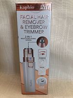 Front view of product box showing product name, 2-in-1 multi-functional design with eyebrow trimmer and facial hair remover, USB rechargeable.