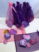 Five purple and pink mesh loot bags, each containing various keychains and accessory sets arranged on a flat surface.
