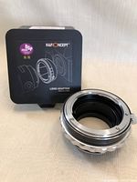 Lens adapter in front of its original black metal box with branding and award sticker.