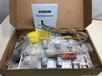 Opened box showing Staresso Glass Bottle Cutter Kit components organized in plastic bags with instruction manual on top