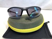 Men’s Ironman sunglasses seated on top of the zippered protective case showing the front face of the glasses and part of the case