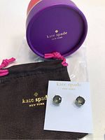Photo of the earrings on a white Kate Spade card with brown pouch and purple round box in background.