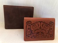 Two wallets side by side, one smooth brown leather, one brown with black tribal design.
