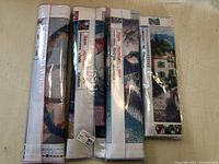 Four sealed diamond painting kits standing vertically, showing edges of canvases and packaging in clear plastic.