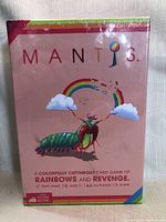 Front of new unopened Mantis card game box showing colorful mantis insect, rainbow, and clouds on pink background