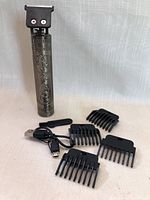 Mini rechargeable hair clipper with four black detachable guard combs and a USB charging cable laid out on white fabric.