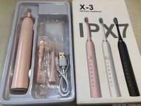 Pink rechargeable electric toothbrush with two extra brush heads and a USB charging cable in the package. Next to the box showing product info for the X-3 model with IPX7 waterproof rating available in three colors.