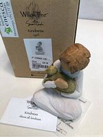 Willow Tree Kindness Girl figurine shown with box and card, viewed from the side and partially top angle showing the figure holding a small green animal.