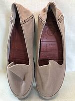 Top view of lightly beige canvas Crocs slip-on shoes showing stitched upper with brown insole and Crocs logo.