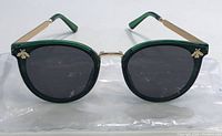 Front view of women's sunglasses showing round dark tinted lenses in translucent dark green plastic frame with gold bridging and bee-shaped embellishments on the top corners.