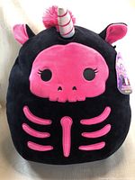 Front view of black unicorn skeleton Squishmallow plush with bright pink skeleton design and horn detail.