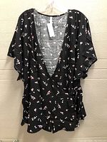 Front view of black floral blouse showing V-neck, flutter sleeves, and waist tie detail.