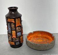 Overview of black and orange ceramic vase next to a textured ceramic ashtray with orange interior