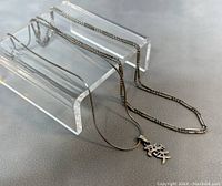 Two sterling silver necklaces displayed on a clear acrylic stand, showing the chain designs and the Chinese character pendant on one necklace.