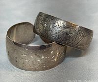 Two small 925 sterling silver open cuff bangles stacked on each other showing engraved floral and leaf patterns.