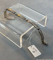 Silver bracelet displayed on clear acrylic stand showing the curved linked segments and attached price tag.
