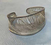 Close-up image of a 925 silver open cuff bangle showing intricate filigree feather-like wire design with minor surface wear.