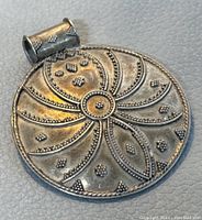 Front view of round silver pendant highlighting textured swirling floral pattern with beaded accents and cylindrical bail marked 925