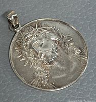 Front close-up view of the round silver pendant showing Jesus crowned with thorns, signs of minor wear visible on surface.
