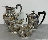 Set of four silver plated items: tea/coffee pot, pitcher, sugar bowl, creamer. Displayed together.