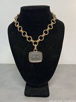 Front view of the gold-tone Art Deco chain necklace with a rectangular carved lion pendant, displayed on a black bust.