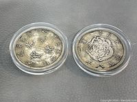Two Chinese silver coins shown front and back with dragon and Chinese character designs in clear protective cases.