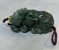 Close-up of the dark green natural Hetian jade carved pendant showing sculpted mythical creature design and polished finish.