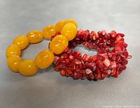 Yellow chunky bead bracelet and two coral chip stone bracelets laid flat showing shape and color.