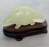 Side view of pale green jade armadillo figure on dark wooden base showing detailed carving and polished finish.