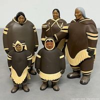 Five Inuit family dolls of varying sizes in traditional clothing, standing side by side on a grey surface.