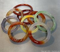 Ten natural jade bangles in various natural colors and two sizes arranged on a light surface, showcasing variety and condition