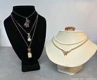 Five necklaces and one pendant/brooch displayed on two necklace busts showing variety and design details of the lot.