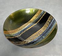 Front of the round copper dish with abstract enameled design in green, black, and gold colors.