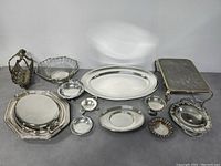 Wide shot showing all silver plated trays, dishes, and baskets included in the lot on a grey surface.