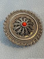 Close-up image of vintage 925 silver brooch showing detailed filigree and red center stone on a light leather surface.
