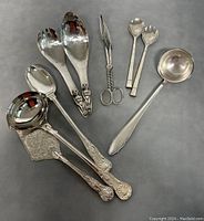 Full set of vintage serving cutlery including ACME First Nations Kwakiutl silver plated salad servers and additional utensils with various designs and details.