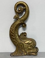 Front view of one brass dolphin andiron showing curved tail and raised scales with minor wear