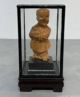 Front view of vintage Chinese carved boxwood child figurine in glass display case on wooden base.