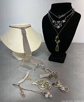 Overall view of jewelry lot displaying necklaces on mannequins and brooches arranged on the surface.