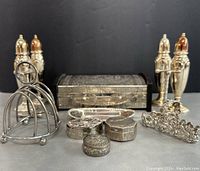 Front view of the lot showing 4 tall matching salt and pepper shakers, a silver toast rack, knife rests, and 4 embossed trinket boxes arranged in front of a rectangular silver box.