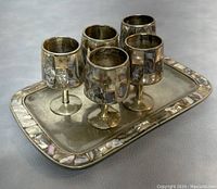 Five silver shot glasses with abalone shell inlays arranged on a matching rectangular silver tray with abalone shell border inlays.