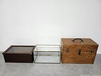 Three vintage storage boxes arranged side by side: wooden display box with glass lid, brass and glass display case, and large wooden box with handle.
