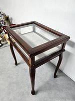Angle view of the vintage wooden display cabinet showing the dark wood frame and glass top.