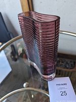 Front angled view showing the wavy form, horizontal decorative lines and the vase's burgundy color on a glass table.