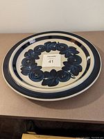 Top view of circular platter showing dark blue floral pattern in ring formation inside a solid blue rim on white background.