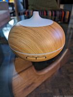 Close-up photo of aroma therapy diffuser showing front wood grain body and white top with control buttons.