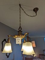 Front view of antique brass chandelier lit, showing frosted bell-shaped glass shades and brass fixture.