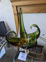 Front and side view of green and amber/gold hand blown art glass centerpiece with elongated spikes and curled shapes on clear base, sitting on glass table.