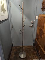 Full view of the metal coat rack showing its height, vertical pole, and arms extending at angles from the pole for hanging.
